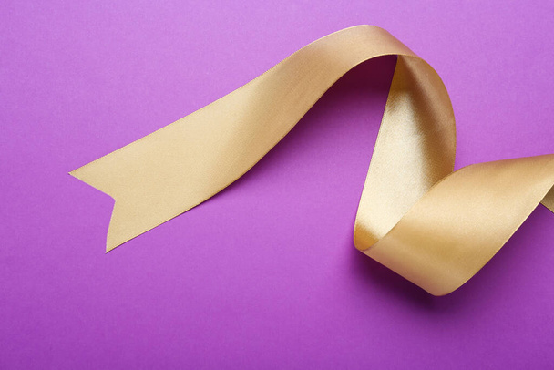 Beautiful golden ribbon on purple background, top view - Фото, изображение