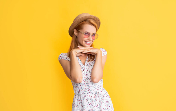 Sarı arka planda hasır şapkalı ve güneş gözlüklü kadın gülümsüyor. - Fotoğraf, Görsel