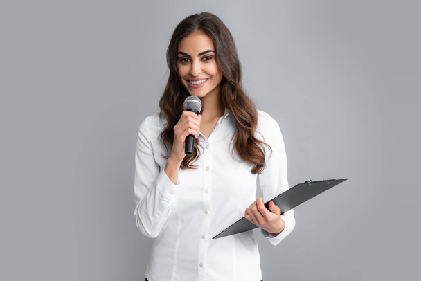 Young female journalist or businesswoman with microphone and clipboard on gray background. - Fotó, kép