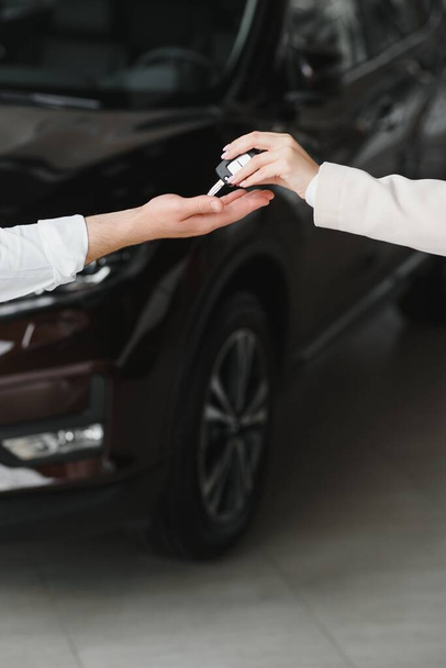 Car sale. Dealer giving key to new owner in auto show or salon, closeup. - Фото, зображення