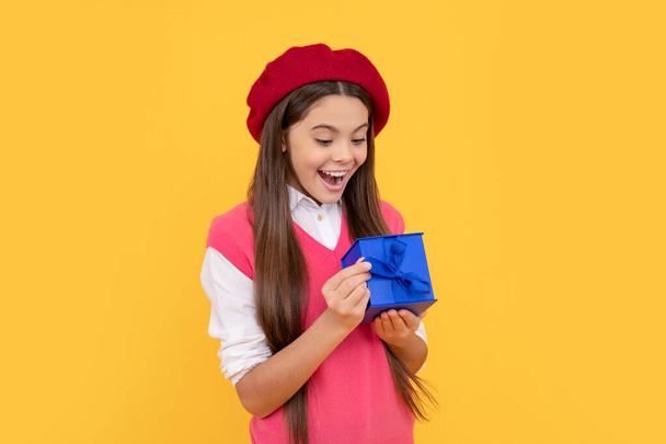 έκπληκτος έφηβος κορίτσι στα γαλλικά μπερέ ανοιχτό δώρο ή κουτί δώρου σε κίτρινο φόντο, ευτυχία - Φωτογραφία, εικόνα
