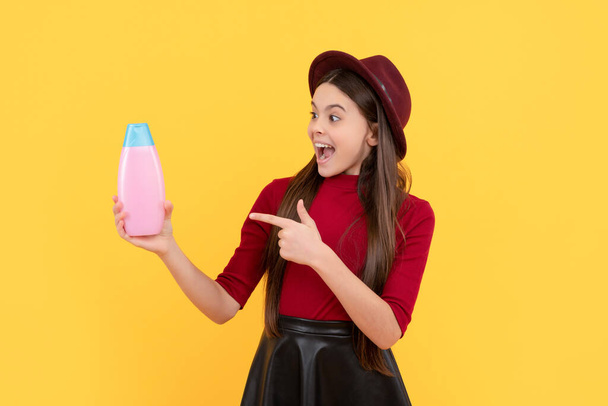 verbaasd kind wijzen vinger op shampoo fles op gele achtergrond, douchegel - Foto, afbeelding