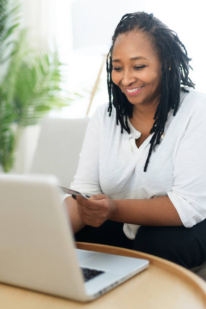 Photo of pretty black woman using laptop at home sofa and buy something on the web - Фото, зображення