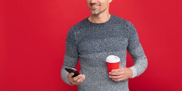 gelukkig knappe man dragen trui hold telefoon en koffiekop, communicatie - Foto, afbeelding