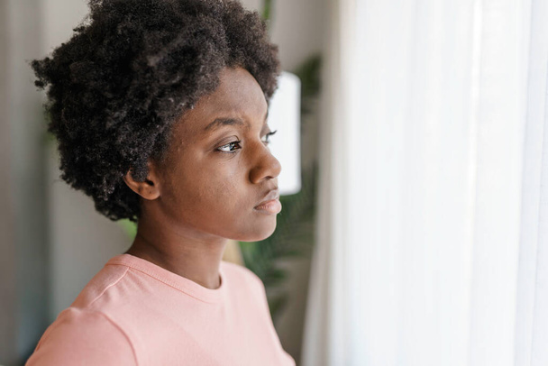 Pensive sad young African American woman look in window - Photo, image
