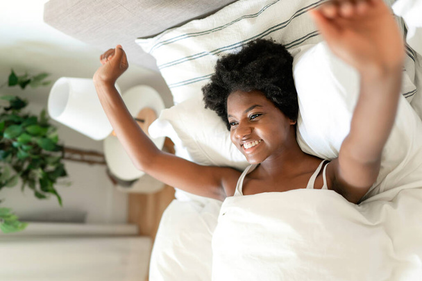 beautiful young African woman in tank top lying in bed - Zdjęcie, obraz