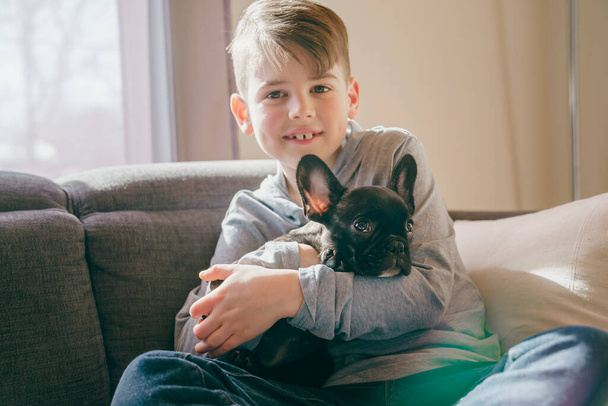 Young Boy with French Bulldog Puppy on the sofa - Fotó, kép