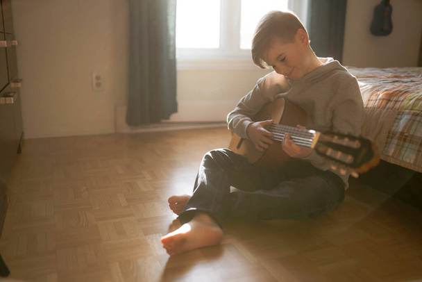A Cheerful Caucasian boy playing guitar on his bedroom - Фото, изображение