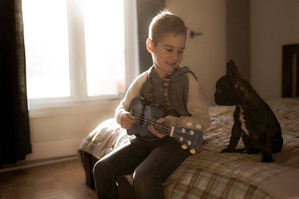 Egy vidám fehér fiú gitározik a hálószobájában. - Fotó, kép