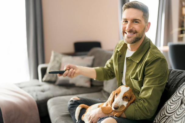 Man Playing With basset Pet Dog At Home sofa listening TV - Foto, imagen