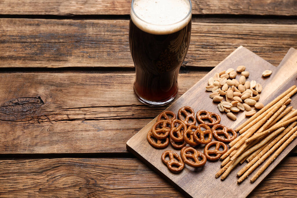 Glass of beer served with delicious pretzel crackers and other snacks on wooden table. Space for text - Zdjęcie, obraz