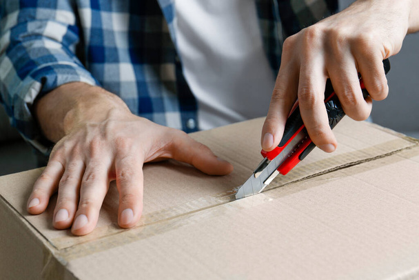 Man using utility knife to open parcel, closeup - Фото, изображение