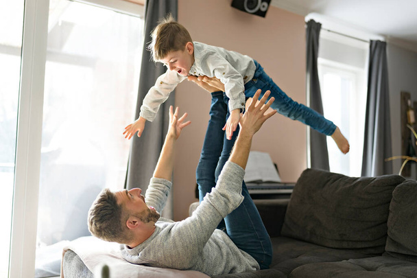 Father or Godfather having fun on the living room sofa At Home flying like a plane - Fotografie, Obrázek