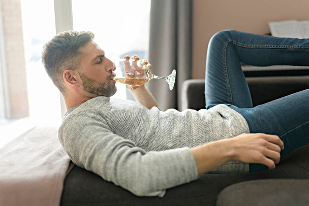 Man drinking wine while having fun lay on sofa - Фото, изображение