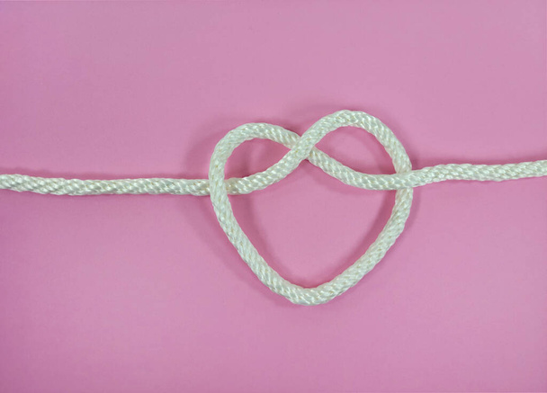 Close up of white rope in a heart shape know on pink background  - Fotoğraf, Görsel