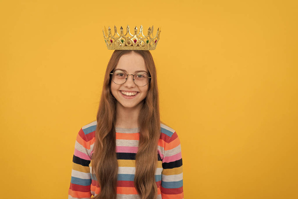 gelukkig kind in bril dragen koningin kroon op gele achtergrond, overwinning - Foto, afbeelding