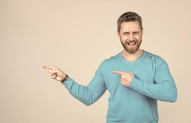 glücklicher reifer Mann mit Bart zeigt mit dem Finger auf grauen Hintergrund mit Kopierraum, Werbung - Foto, Bild