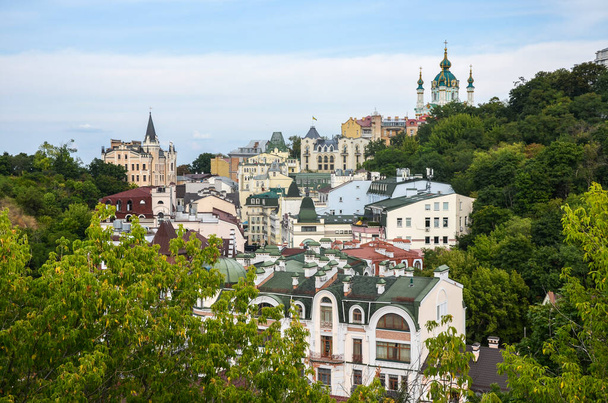 View on St. Andrew's Church and colorful modern residential buildings of Vozdvizhenka district in the historical center of Kyiv, at the Podil  - Foto, afbeelding