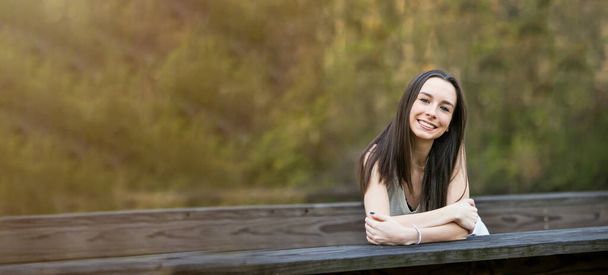 Kaunis onnellinen teini brunette tyttö ulkona nojaten sillalla paikallisessa puistossa onnellinen hänen tulevaisuuden suunnitelmia - Valokuva, kuva