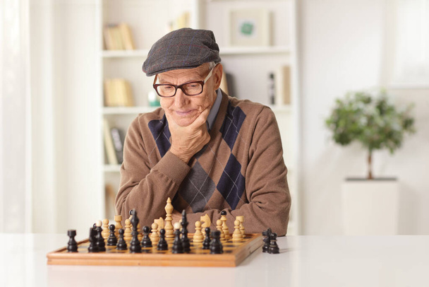 Elderly man playing chess alone at a table at home - Fotó, kép