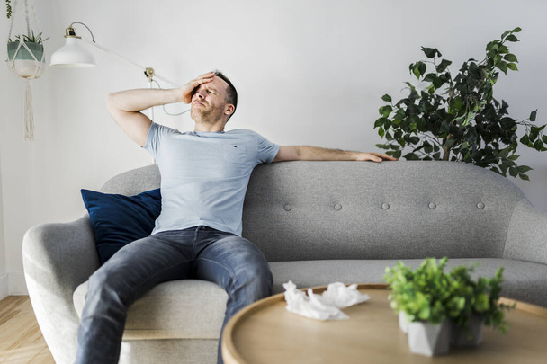 Frustrated handsome man with problem sitting on the couch at home with tissue on the front - Fotoğraf, Görsel