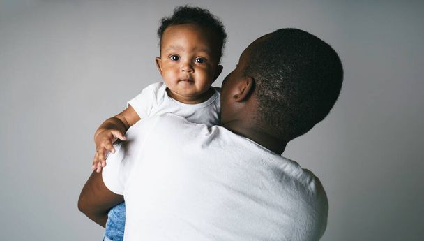 portrait of beautiful african man holding on hands her little son on grey background - Fotografie, Obrázek
