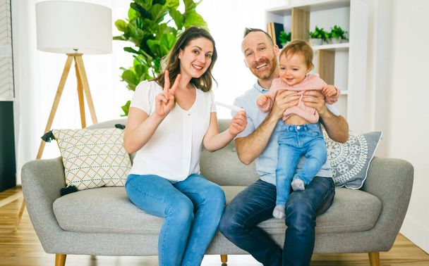 rodina šťastná s těhotenským testem se svou vzrušenou ženou sedí na gauči doma. - Fotografie, Obrázek