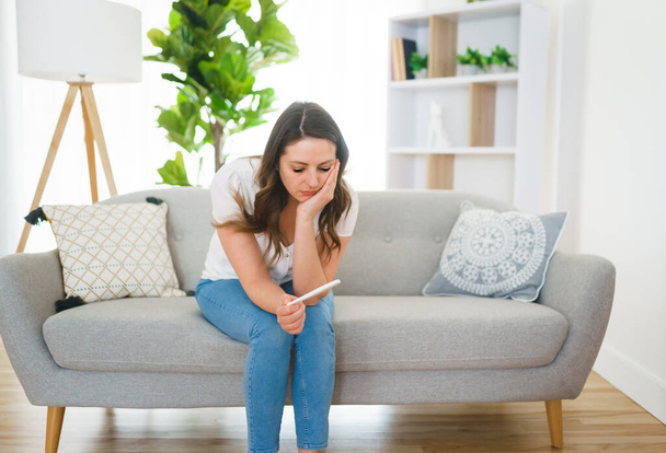 A girl sitting on a couch at home while reading the results of her recent pregnancy test - Fotoğraf, Görsel