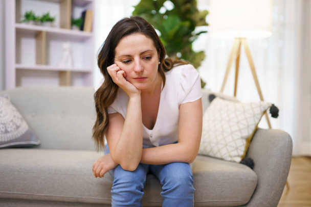 Stressed mature woman sitting on sofa at home look sad - Foto, afbeelding