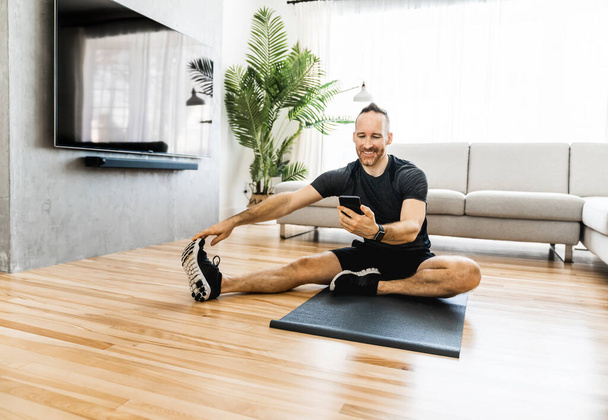 Man on a mat doing some exercise at home using cellphone to help training - Valokuva, kuva