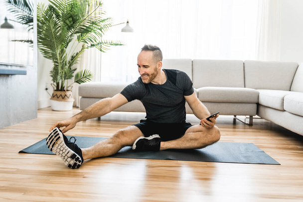 Man on a mat doing some exercise at home using cellphone to help training - Photo, Image
