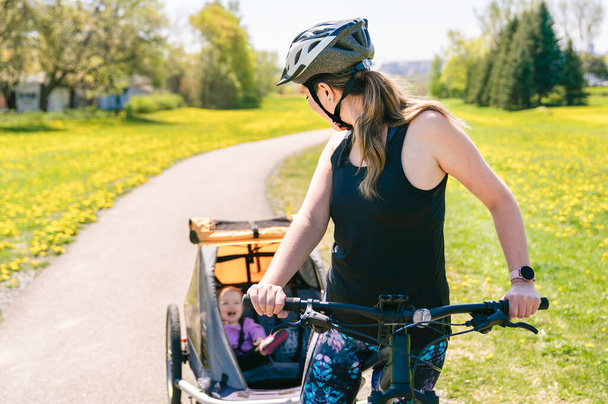 woman riding a bicycle with a baby stroller attached to the bicycle. - Foto, immagini