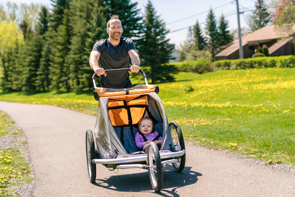man with baby in jogging stroller running outside in summer season - Photo, image