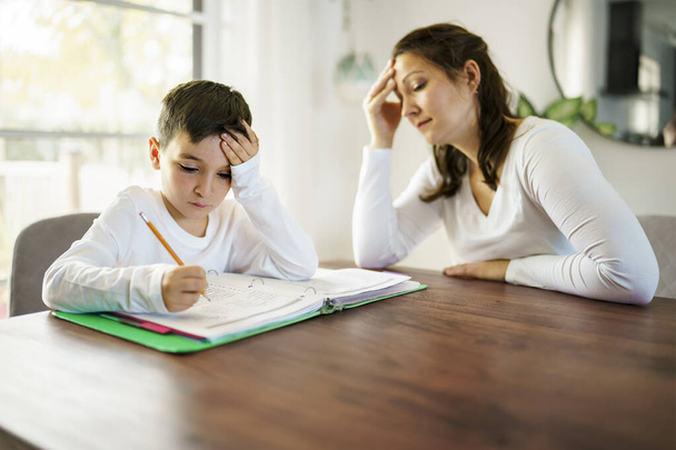 mother teaching bored son and helping with homework at home - Photo, image