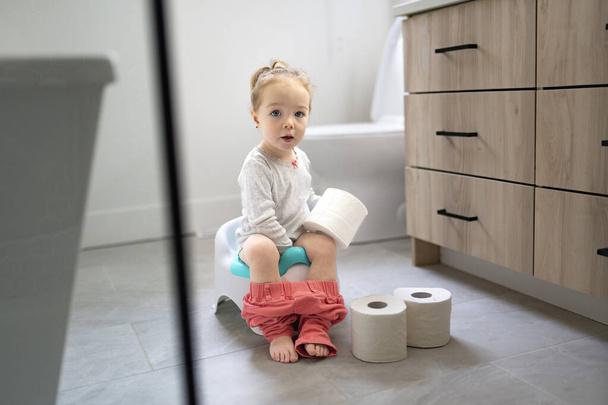 Adorable young baby child sitting and learning how to use the toilet with toilet paper on hand - Foto, Bild