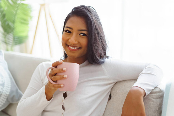 美しい笑顔アメリカ人女性に座っていますソファコーヒーを飲みながら - 写真・画像