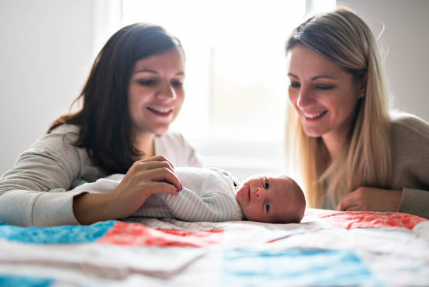 Two friend girl with a newborn baby on bed - Photo, Image
