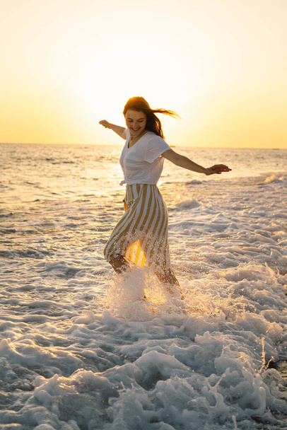 Młoda szczęśliwa kobieta tańczy kręcąc się po morzu w żółtej, trzepoczącej sukience. - Zdjęcie, obraz