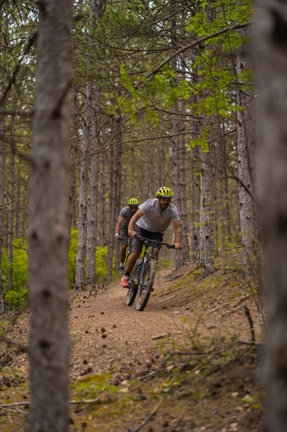 Two male friends are racing each other in the forest while riding their bikes - Фото, зображення