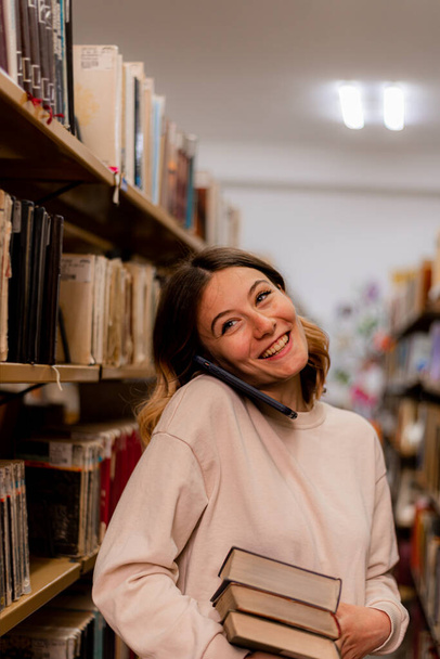 Girl smiling and talking on the phone while holding books - Фото, зображення