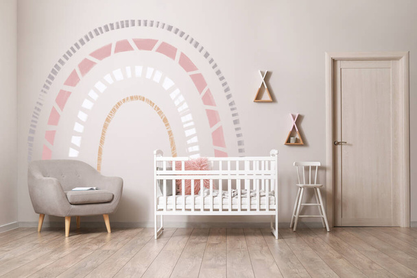 Interior of children's room with crib, armchair and light wall with painted rainbow - Foto, Imagem