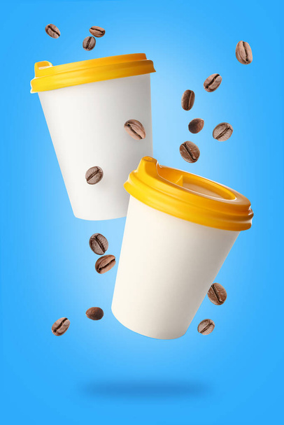 Flying takeaway coffee cups and beans on blue background - 写真・画像