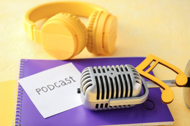 Microphone, headphones, notebook and sheet of paper with word PODCAST on yellow background, closeup - Photo, Image
