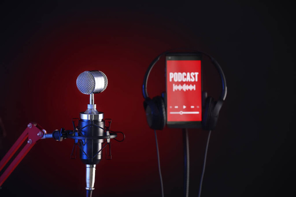 Микрофон, мобильный телефон со словом PODCAST на экране и наушники на темном фоне, крупный план - Фото, изображение