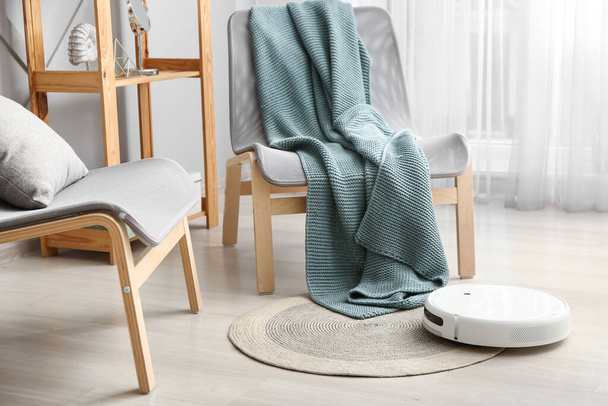 Aspirador robot moderno en alfombra cerca de sillas en la sala de estar - Foto, Imagen