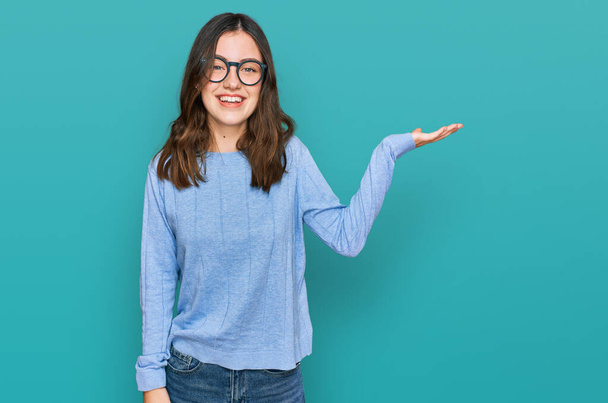 Young beautiful woman wearing casual clothes and glasses smiling cheerful presenting and pointing with palm of hand looking at the camera.  - Φωτογραφία, εικόνα