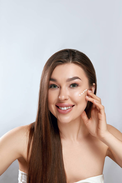 Beauty Face. Beautiful Woman With Natural Makeup Applying Cream To Her Face . Closeup Portrait Of Model Girl With Healthy Smooth Facial Skin - 写真・画像