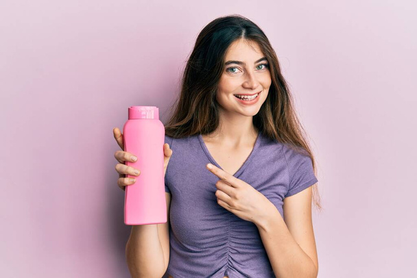 Young caucasian woman holding shampoo bottle smiling happy pointing with hand and finger  - Фото, зображення
