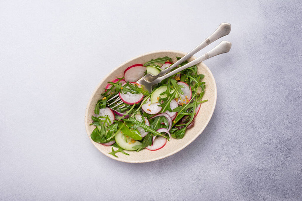 Healthy and tasty vegan food. Top view of light salad with radish, cucumber, onion, fresh green leaves and mustard sause on grey concrete background - Fotoğraf, Görsel