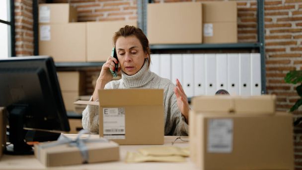Middelbare leeftijd Spaanse vrouw e-commerce zakenman praten op de smartphone in het magazijn kantoor - Foto, afbeelding